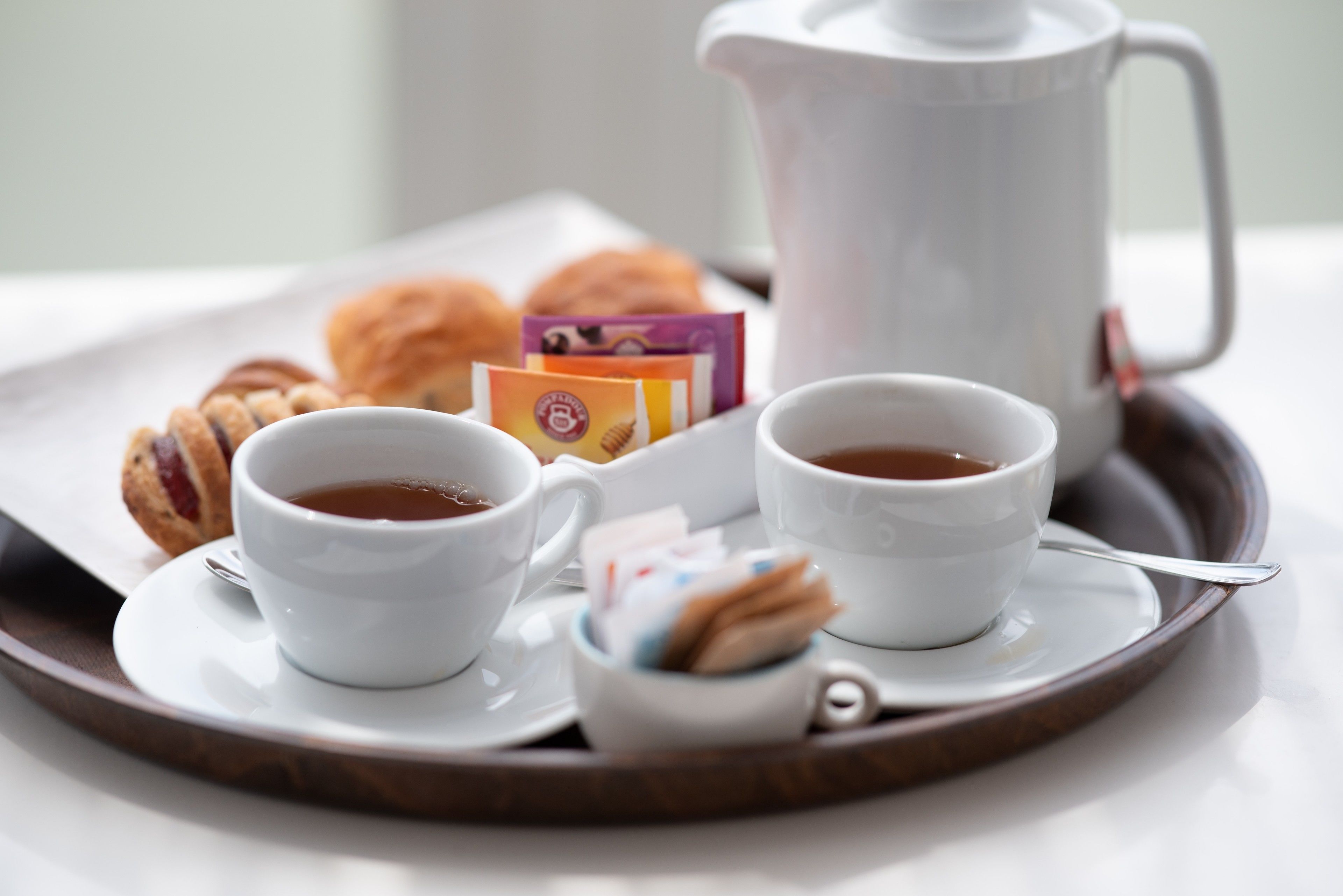 Un plateau avec deux tasses de thé, une théière, des pâtisseries et des sachets de thé.