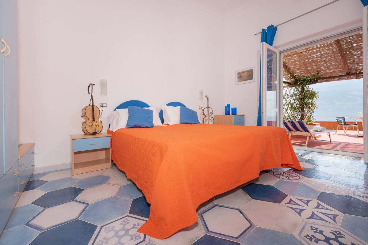 Ein Schlafzimmer mit einem Bett, einer Gitarre, einem Nachttisch und Blick ins Freie.
