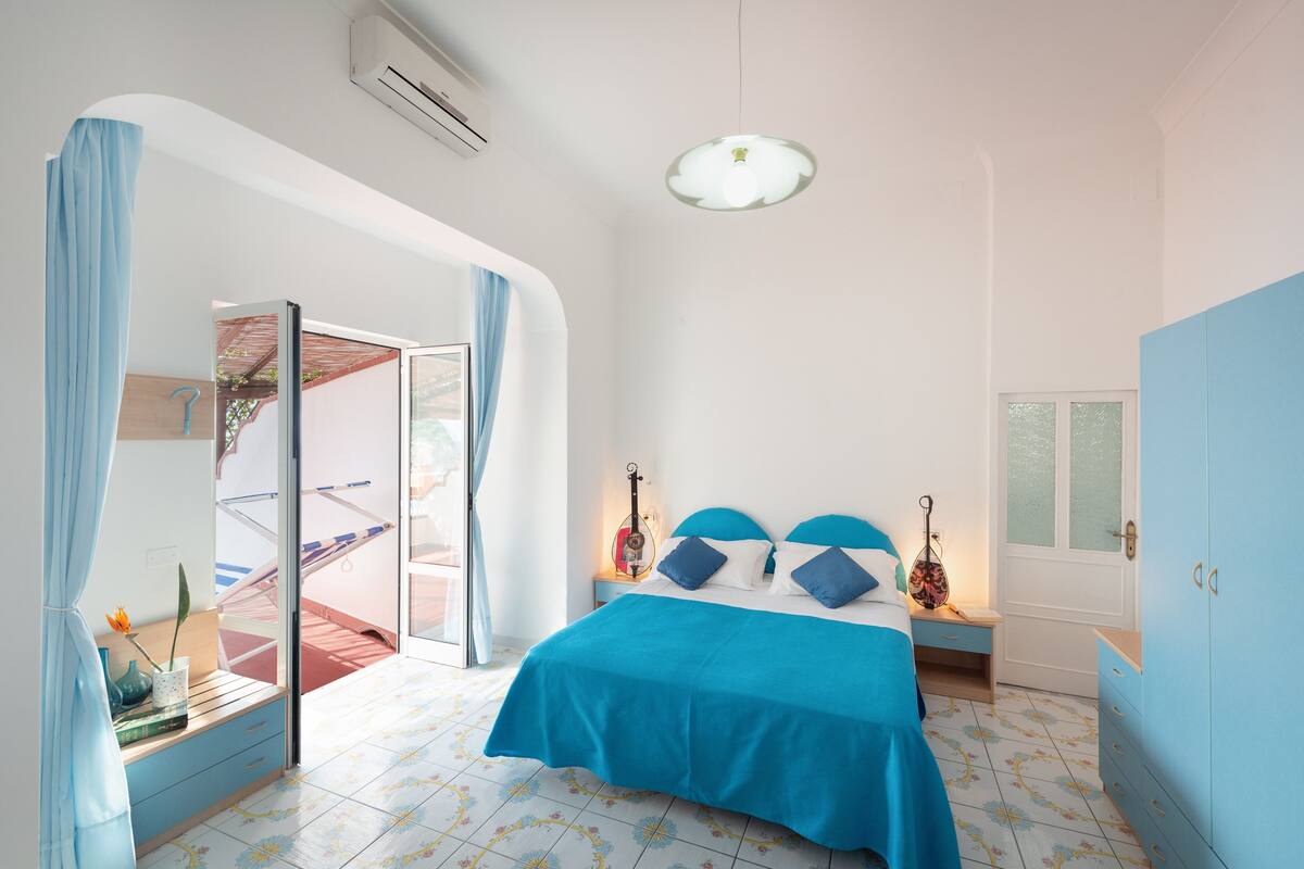 Ein Schlafzimmer mit einem Bett, einem Nachttisch, einer Gitarre und einem Fenster.