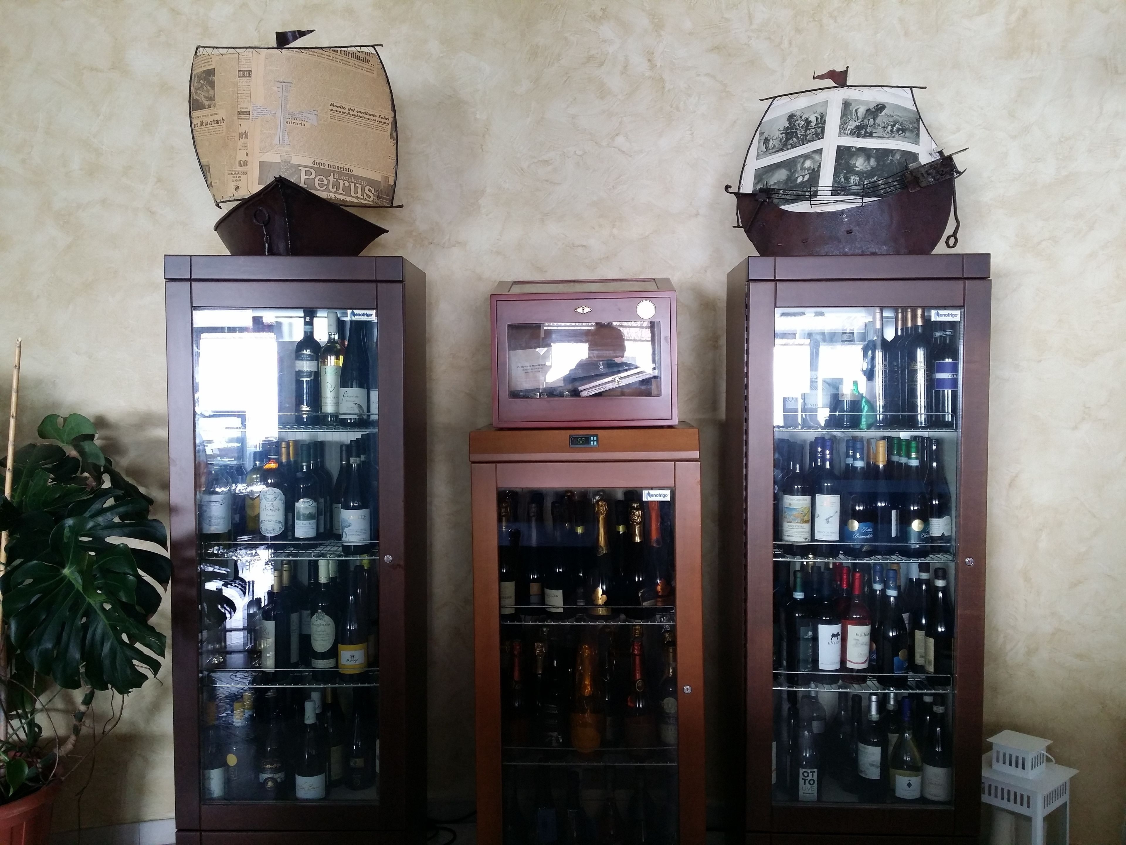 Tres armarios altos de color oscuro con puertas de cristal, cada uno conteniendo varias botellas. Un televisor peque ño con marco rosa está situado encima del armario central.