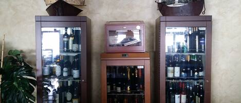 Tres armarios altos de color oscuro con puertas de cristal, cada uno conteniendo varias botellas. Un televisor pequeño con marco rosa está situado encima del armario central.