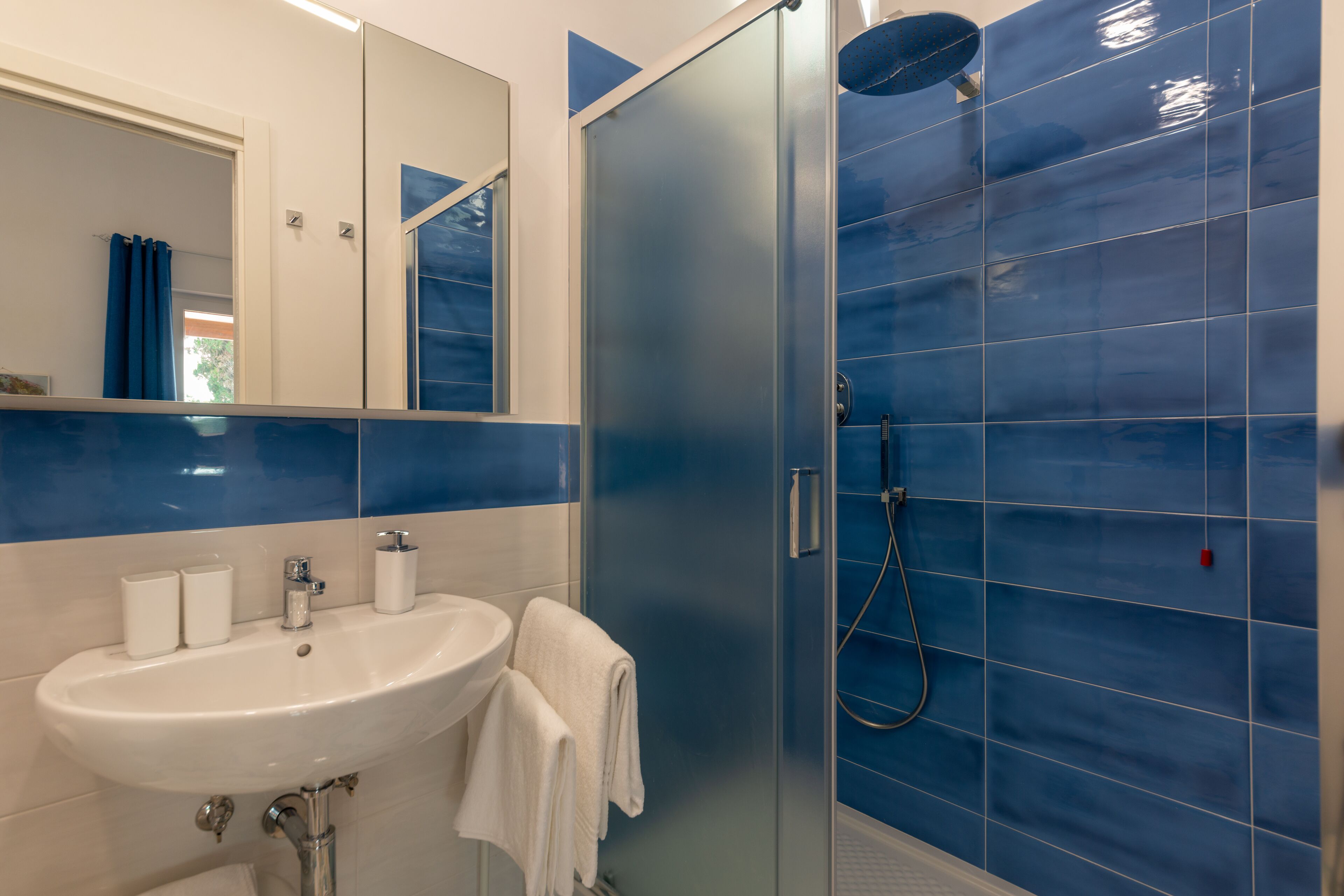 Une salle de bain avec un lavabo blanc, un miroir et des murs recouverts de carreaux bleus.