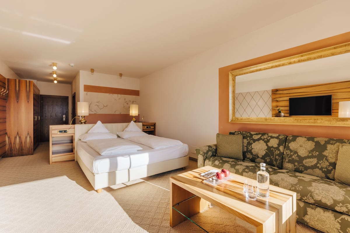 A hotel room with a bed, bedside tables, a sofa, a TV, and a mirror.