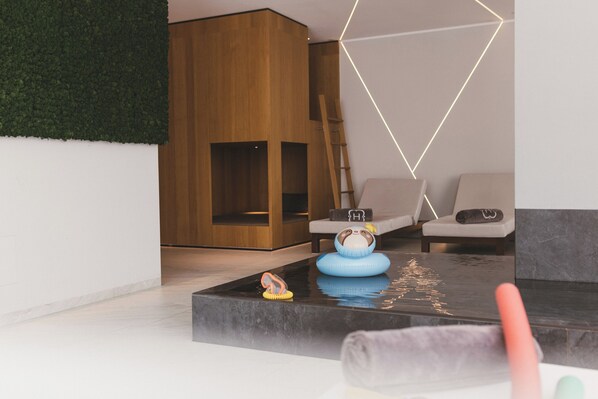 A modern living room with a wooden wall, a sofa, a coffee table, and a small rug. - Hotel Hohenwart (Schenna)