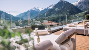 A sunlit outdoor seating area with a view of snow-capped mountains. - Hotel Hohenwart (Schenna)