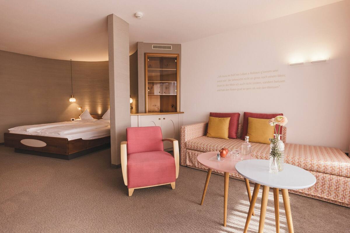 A modern room with a bed, a red chair, a sofa with cushions, a small table, and a bookshelf.