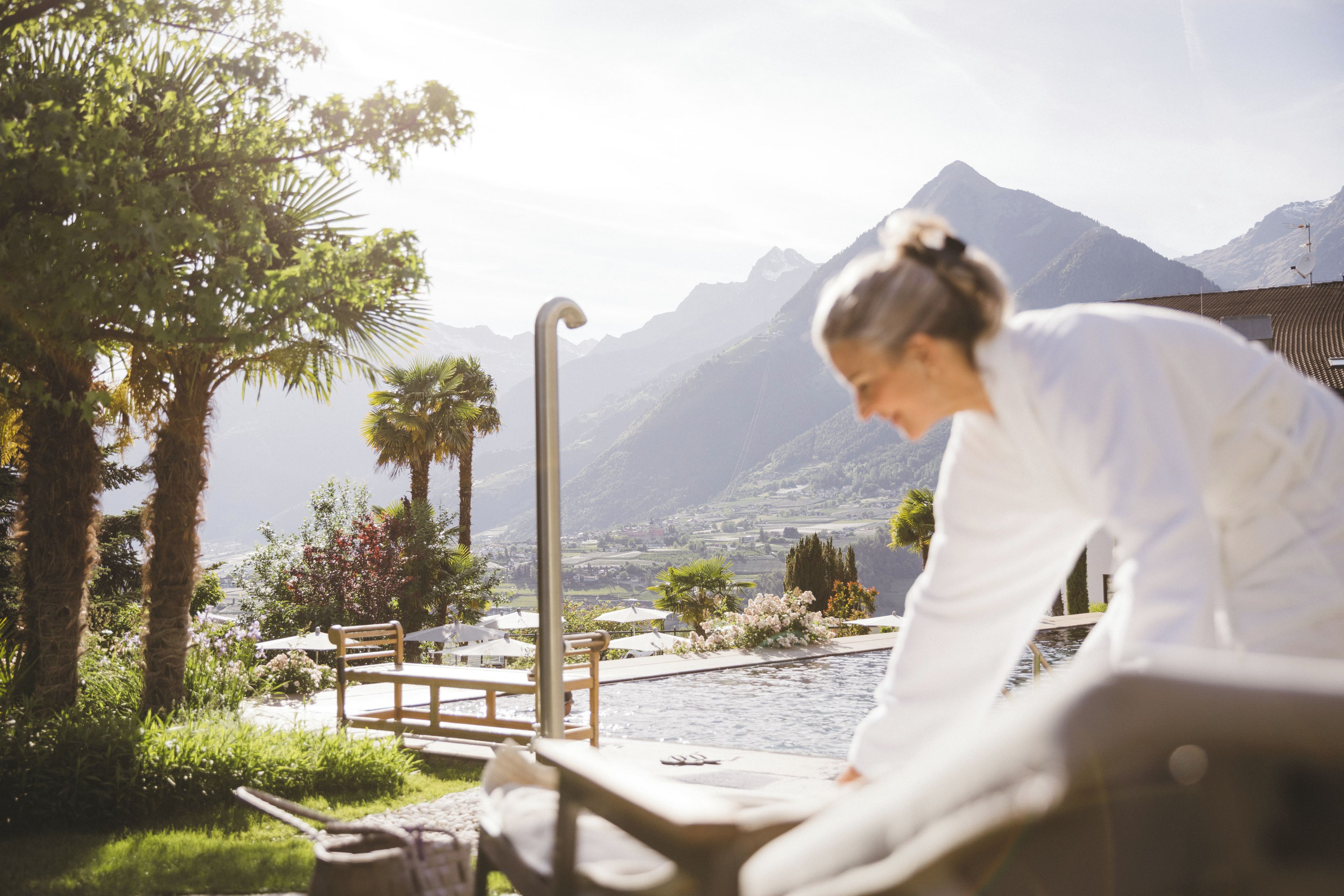 A person stretching outdoors with a view of mountains and a pool area in the background.