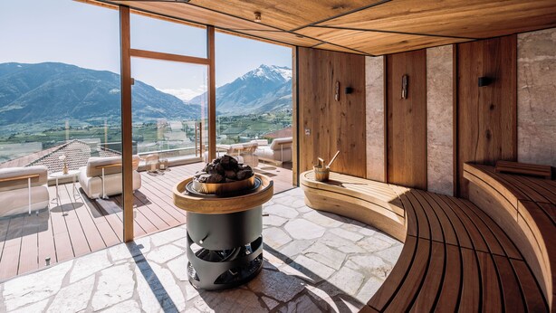 A modern interior with a stone floor, wooden furniture, and a large window offering a mountain view. - Hotel Hohenwart (Schenna)
