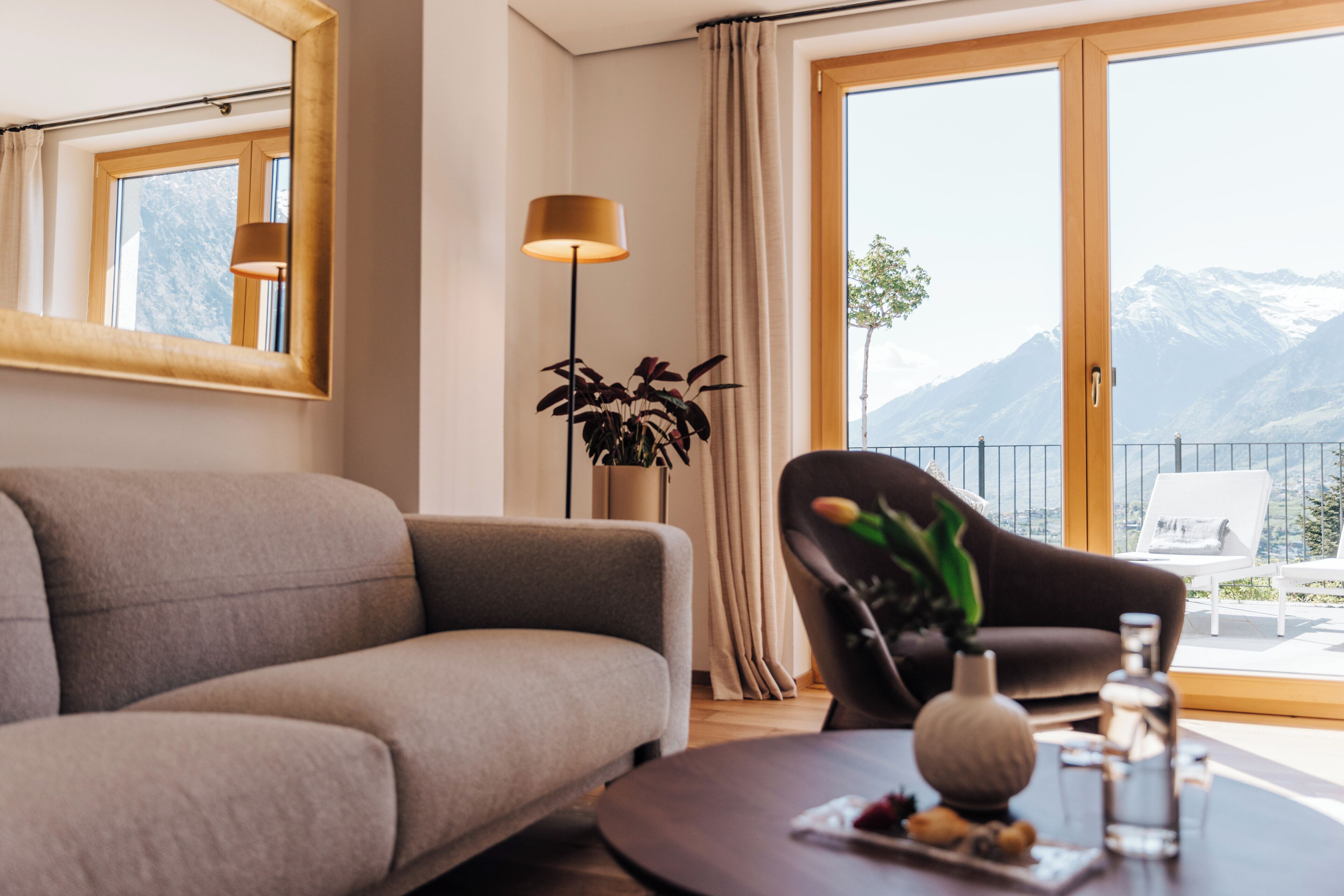 A modern living room with a sofa, a coffee table with a vase and snacks, a floor lamp, and a view of mountains through large windows.