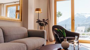 A modern living room with a sofa, a coffee table with a vase and snacks, a floor lamp, and a view of mountains through large windows.