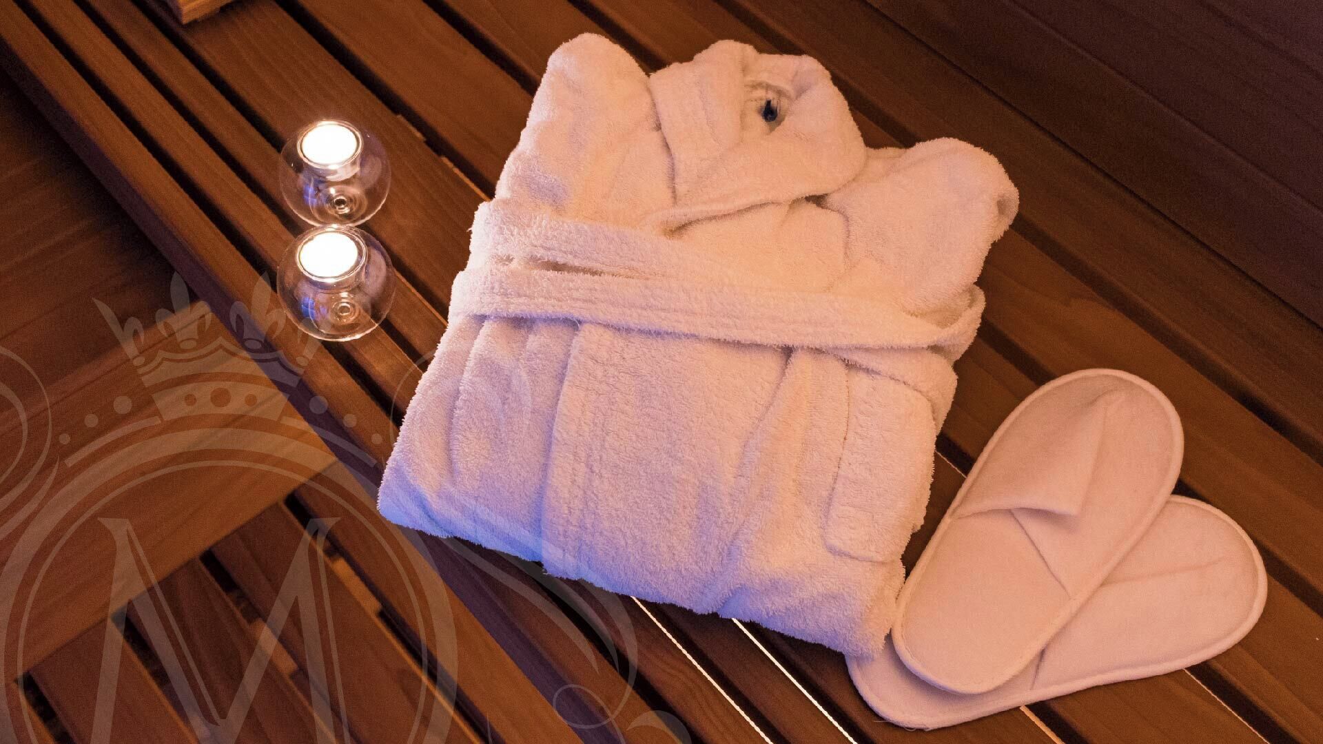 A neatly folded bathrobe and slippers on a wooden bench with two lit candles.