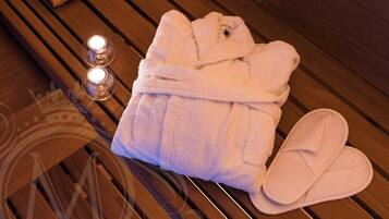 A neatly folded bathrobe and slippers on a wooden bench with two lit candles.