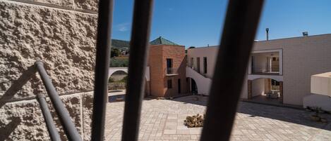 A courtyard with a stone floor, a brick building, and a metal railing.