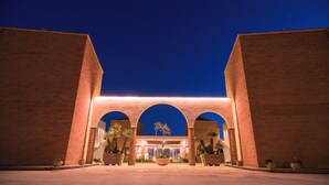 A building with a large arched entrance, potted plants, and a well-lit facade at night. - Il Marchese Hotel & Spa (Sciacca)