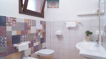 A bathroom with a tiled backsplash, a toilet, a bidet, and a sink.