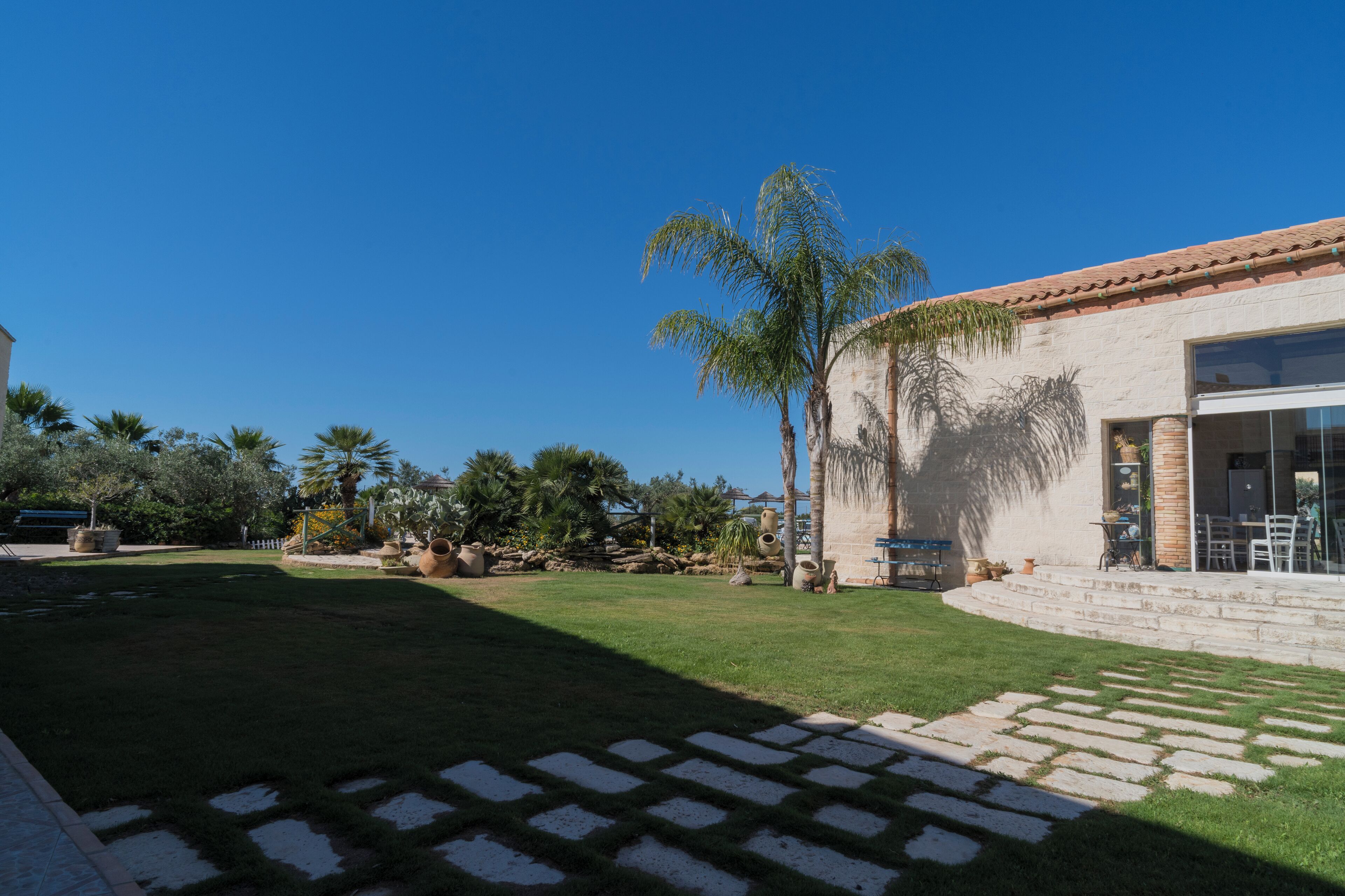 A well-maintained outdoor area with a paved patio, palm trees, and a stone building with large windows.