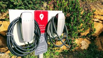 Uma estação de carregamento Tesla com dois pontos de carregamento, rodeada por vegetação.