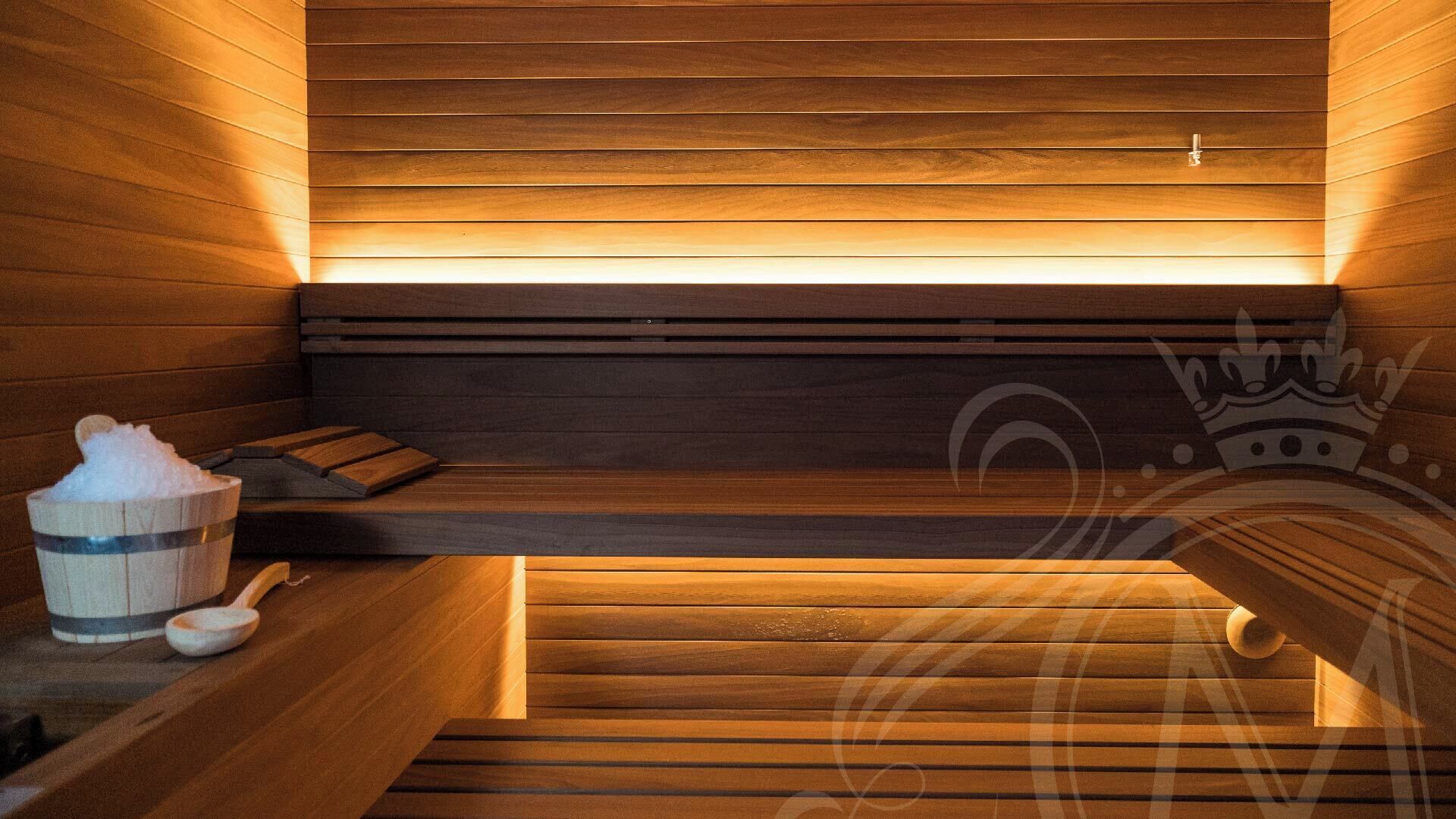 Un sauna avec des bancs en bois, un banc, un seau en bois et une louche en bois.