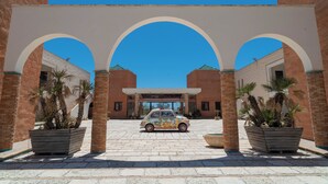 A building entrance with a car parked under an archway, surrounded by potted plants. - Il Marchese Hotel & Spa (Sciacca)