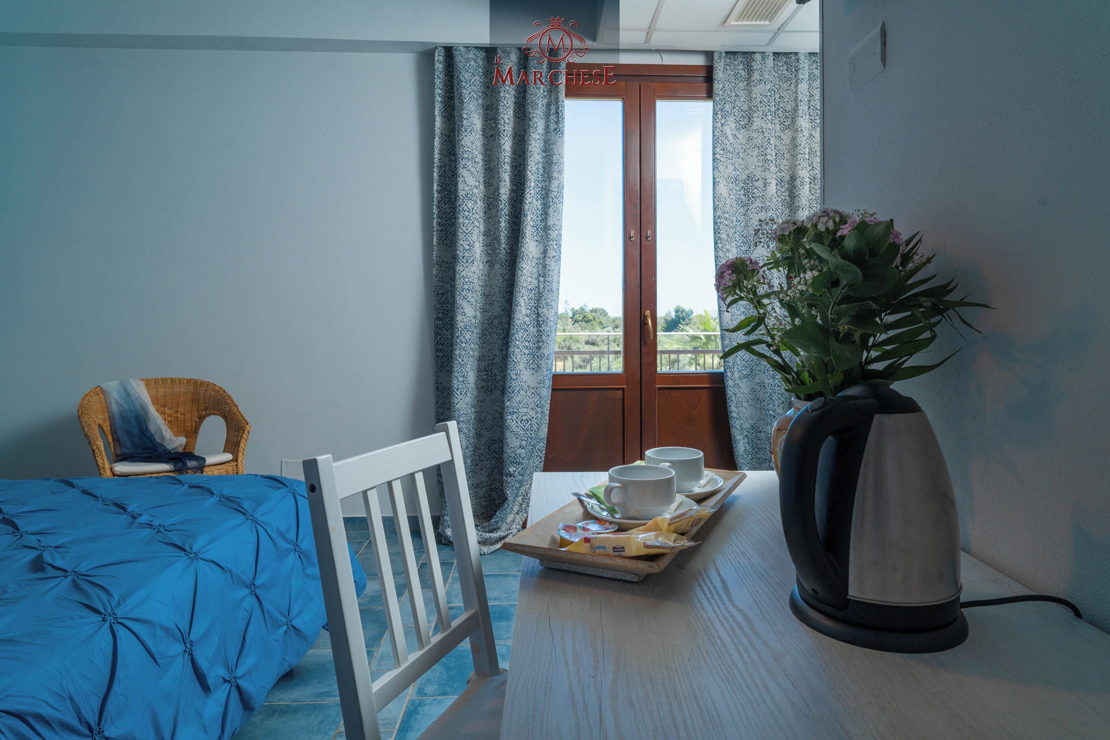 Habitación de hotel con cama, una mesa de comedor con una bandeja de alimentos para el desayuno, un hervidor y una silla.