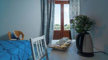 A hotel room with a bed, a dining table with a tray of breakfast items, a kettle, and a chair.