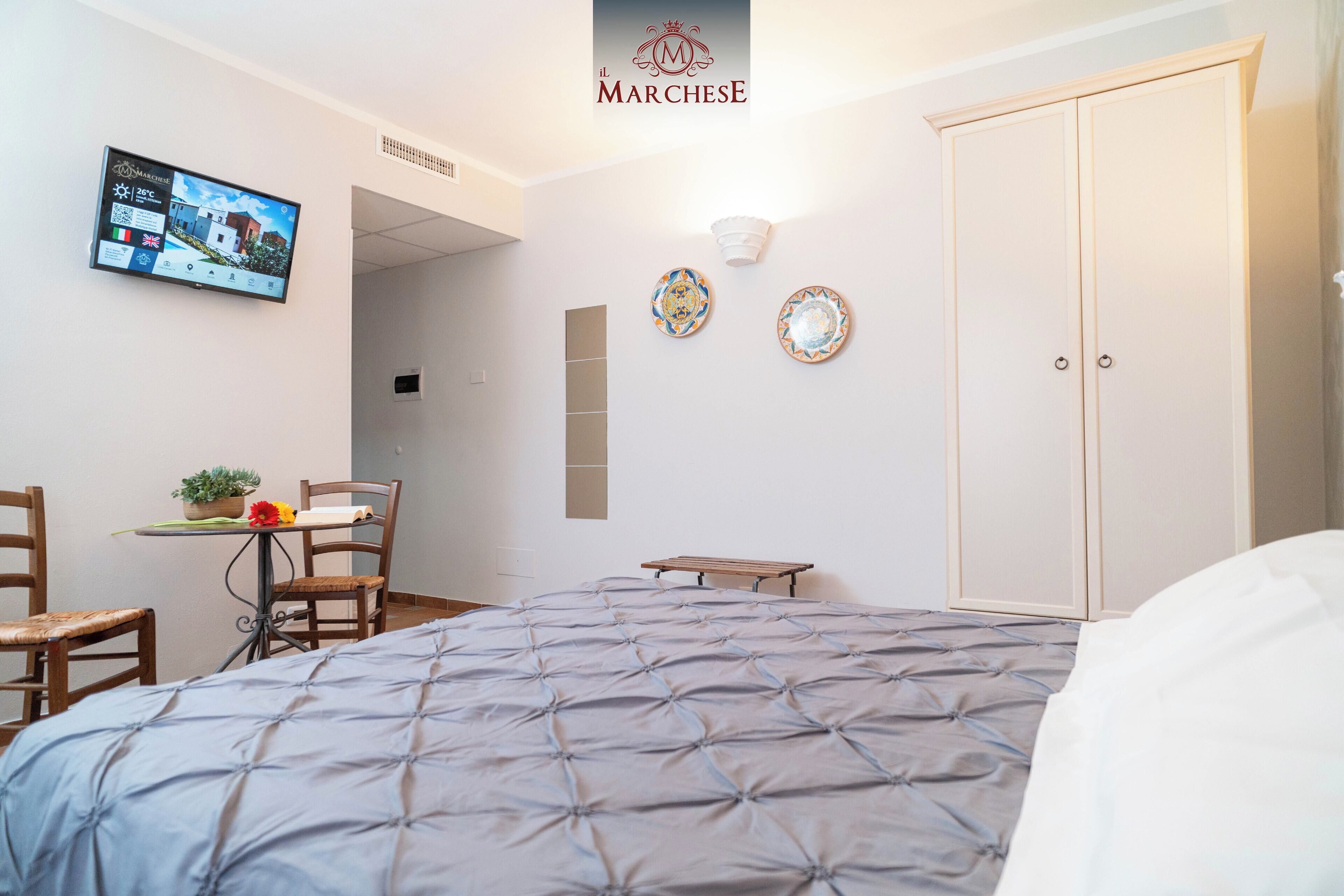 A hotel room with a bed, a desk with a chair, a television, and a wardrobe.