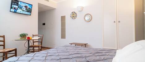 A hotel room with a bed, a desk with a chair, a television, and a wardrobe.