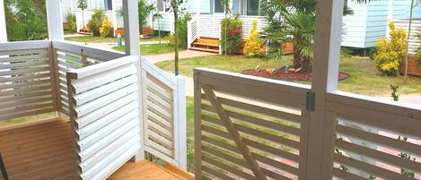 A wooden deck with white railings, a grassy yard with various plants, and a white building in the background.