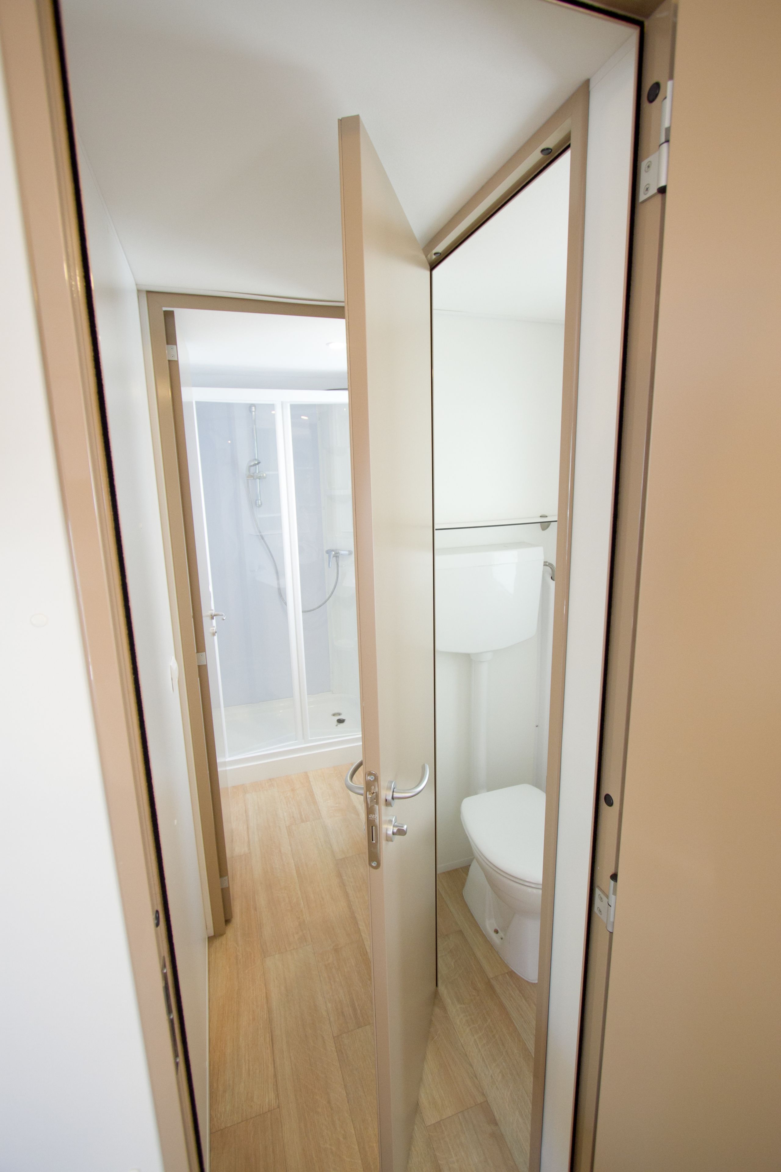 Ein Badezimmer mit Toilette, einer Duschkabine und einer Tür zu einem anderen Raum.