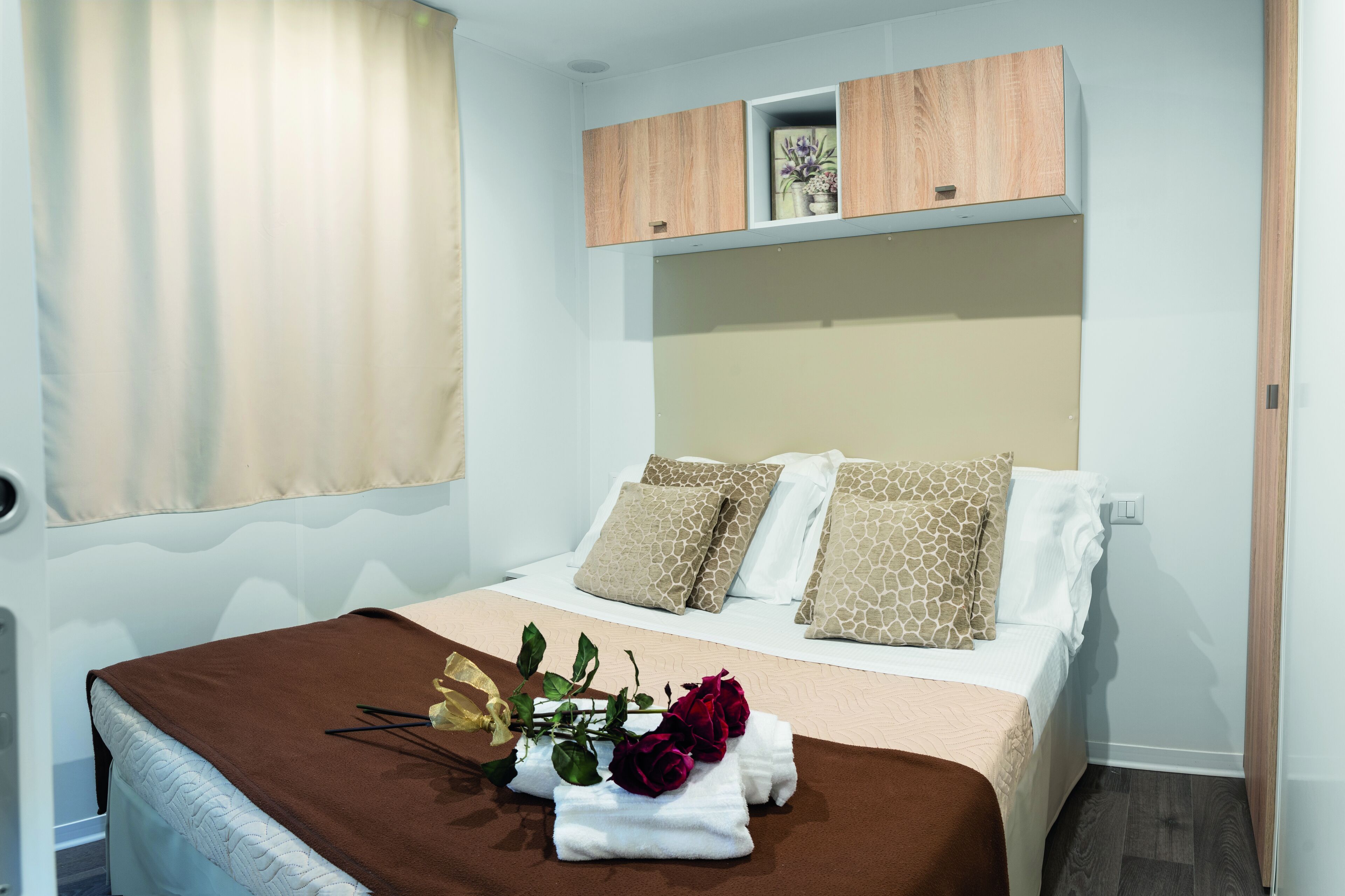 A neatly made bed with a brown blanket, two pillows with a giraffe pattern, and a bouquet of flowers on the bed.