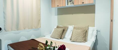 A neatly made bed with a brown blanket, two pillows with a giraffe pattern, and a bouquet of flowers on the bed.