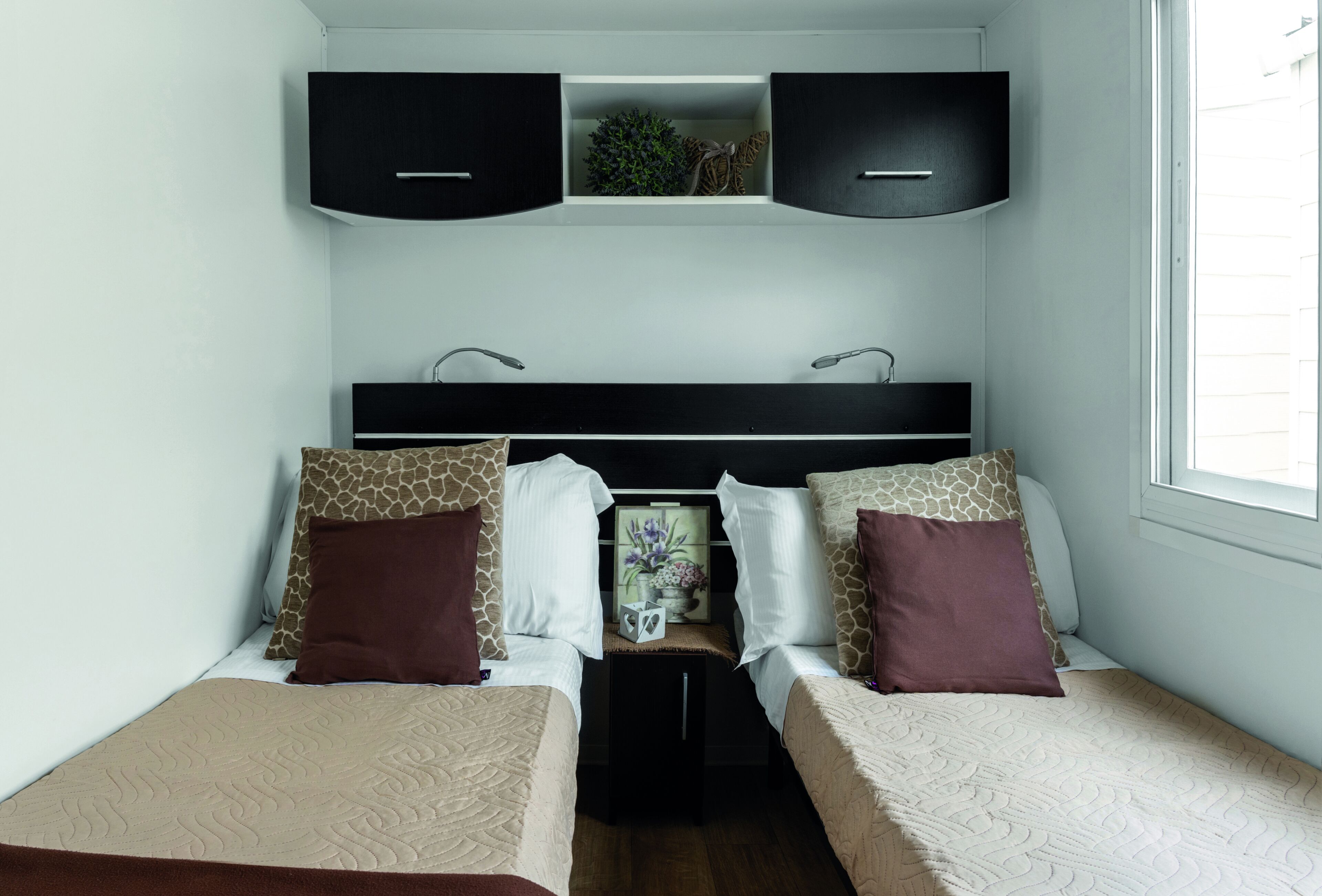 A bedroom with two beds, a nightstand, a dresser, and a window.