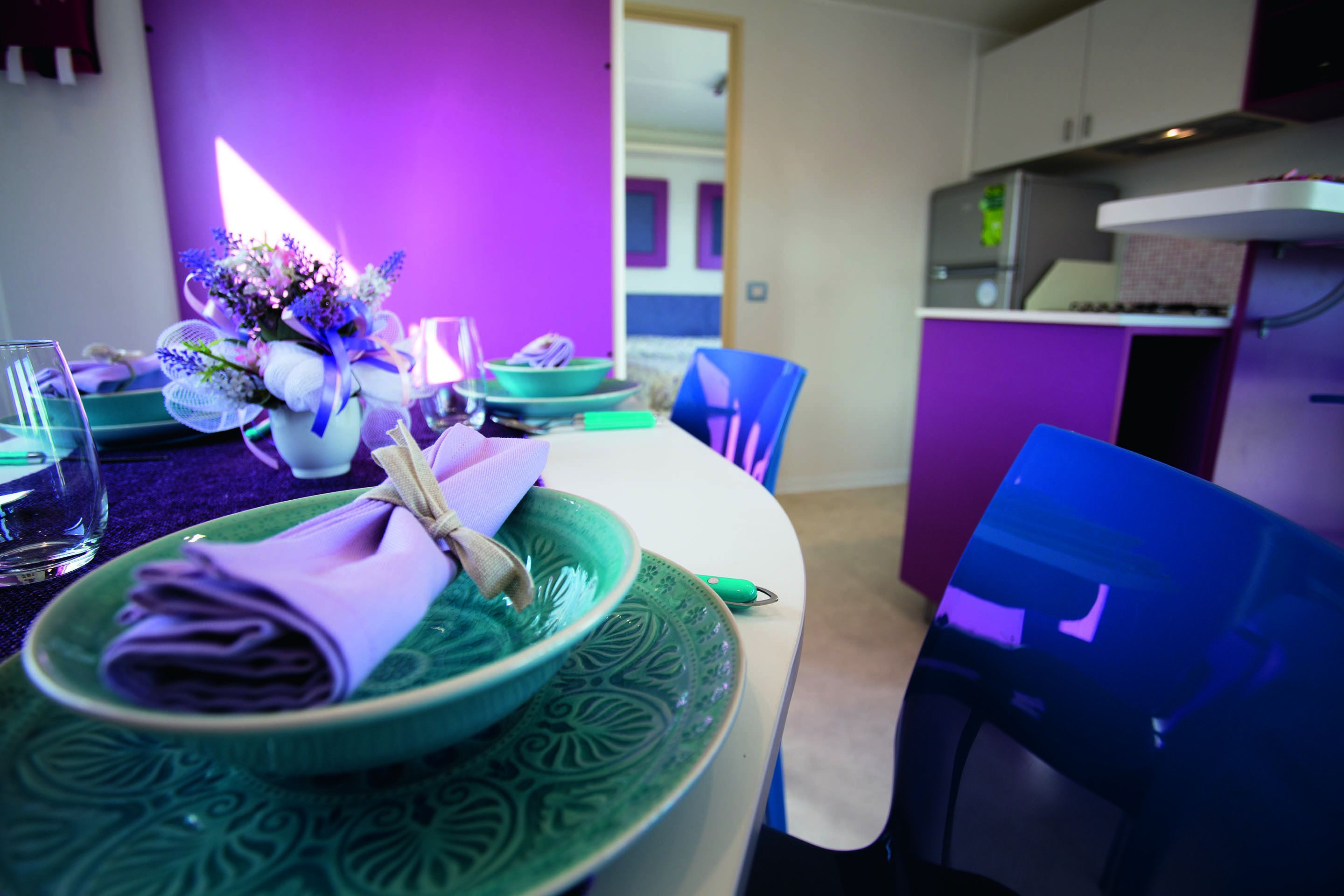 A dining area with a purple wall, green plates, and blue chairs.