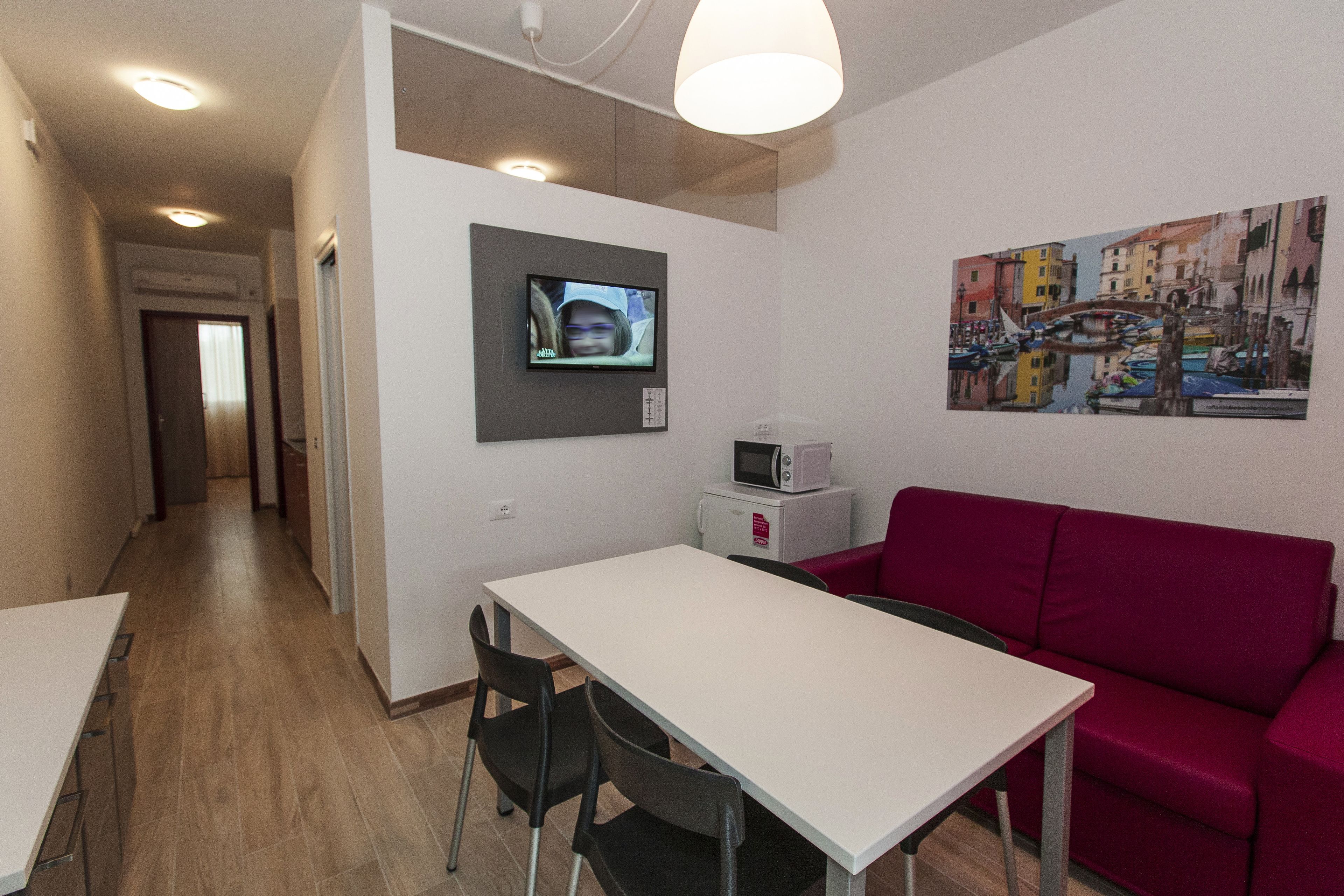 A modern living room with a white table, red sofa, and a flat-screen TV mounted on the wall.