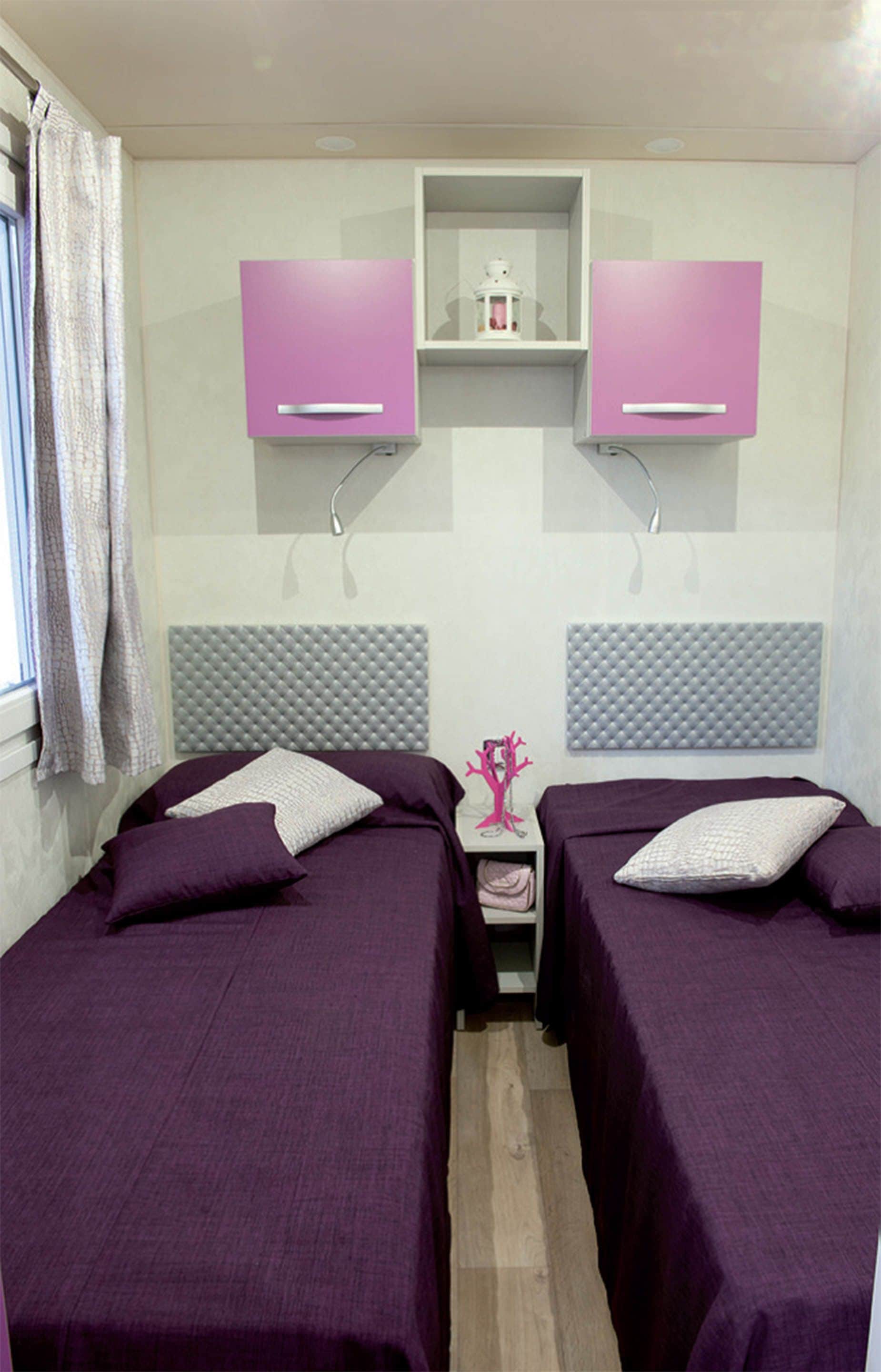Une chambre avec deux lits, chacun doté d’une tête de lit et d’oreillers, et une petite table avec une lampe placée entre les deux.