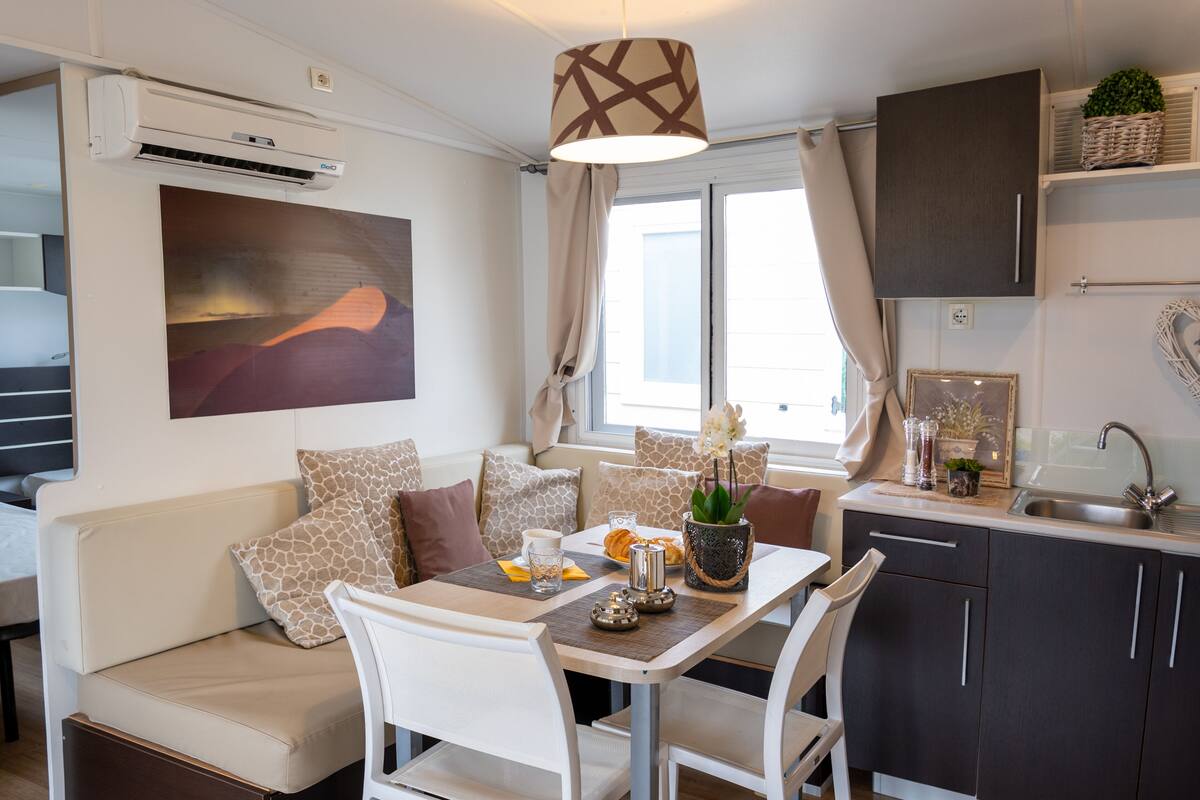 A compact living space with a sofa, dining table, chairs, a kitchen area, and a large window.