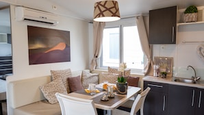 A compact living space with a sofa, dining table, chairs, a kitchen area, and a large window. - Camping Village Internazionale (Chioggia)