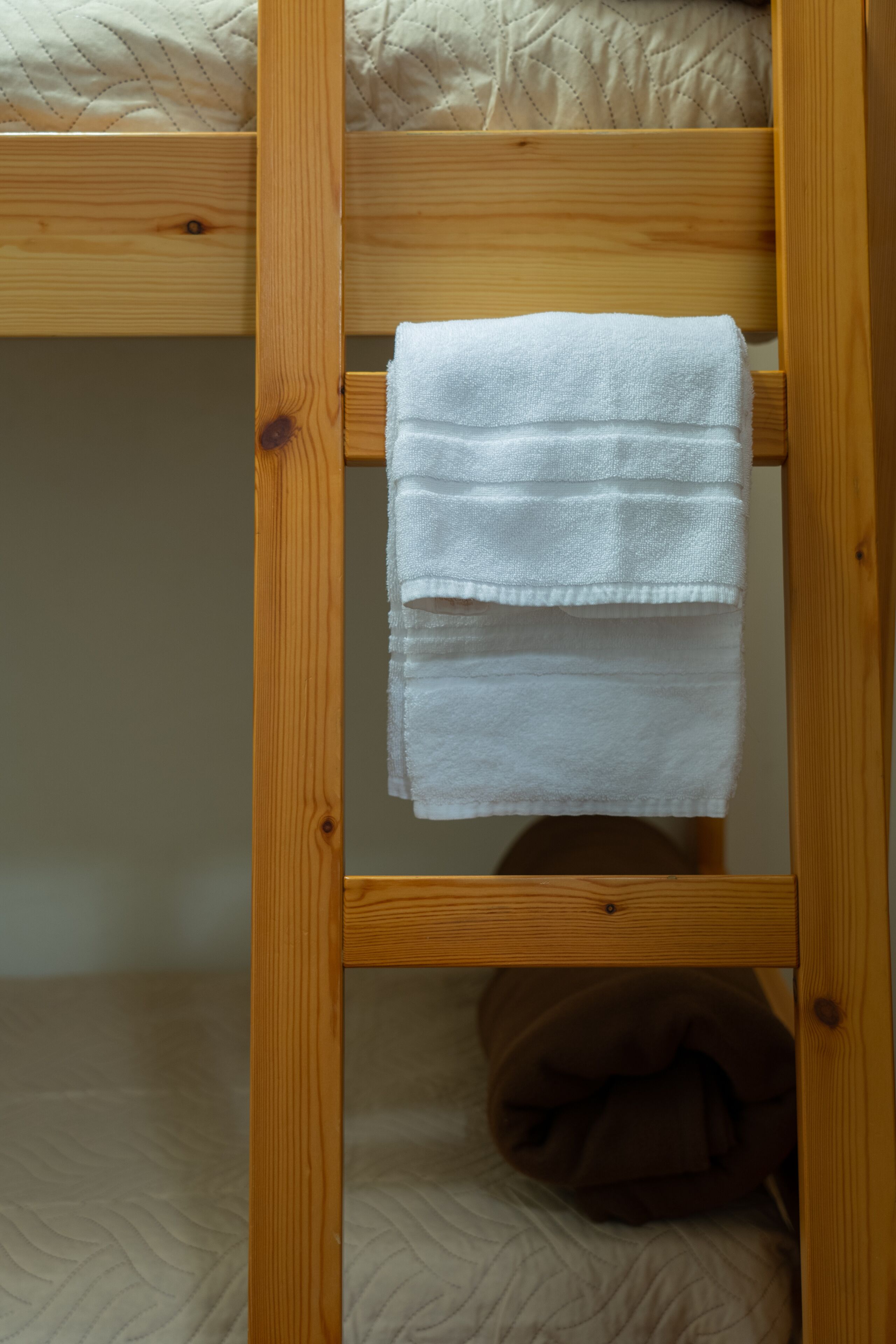 A bunk bed with a wooden ladder and a white towel hanging on the side.