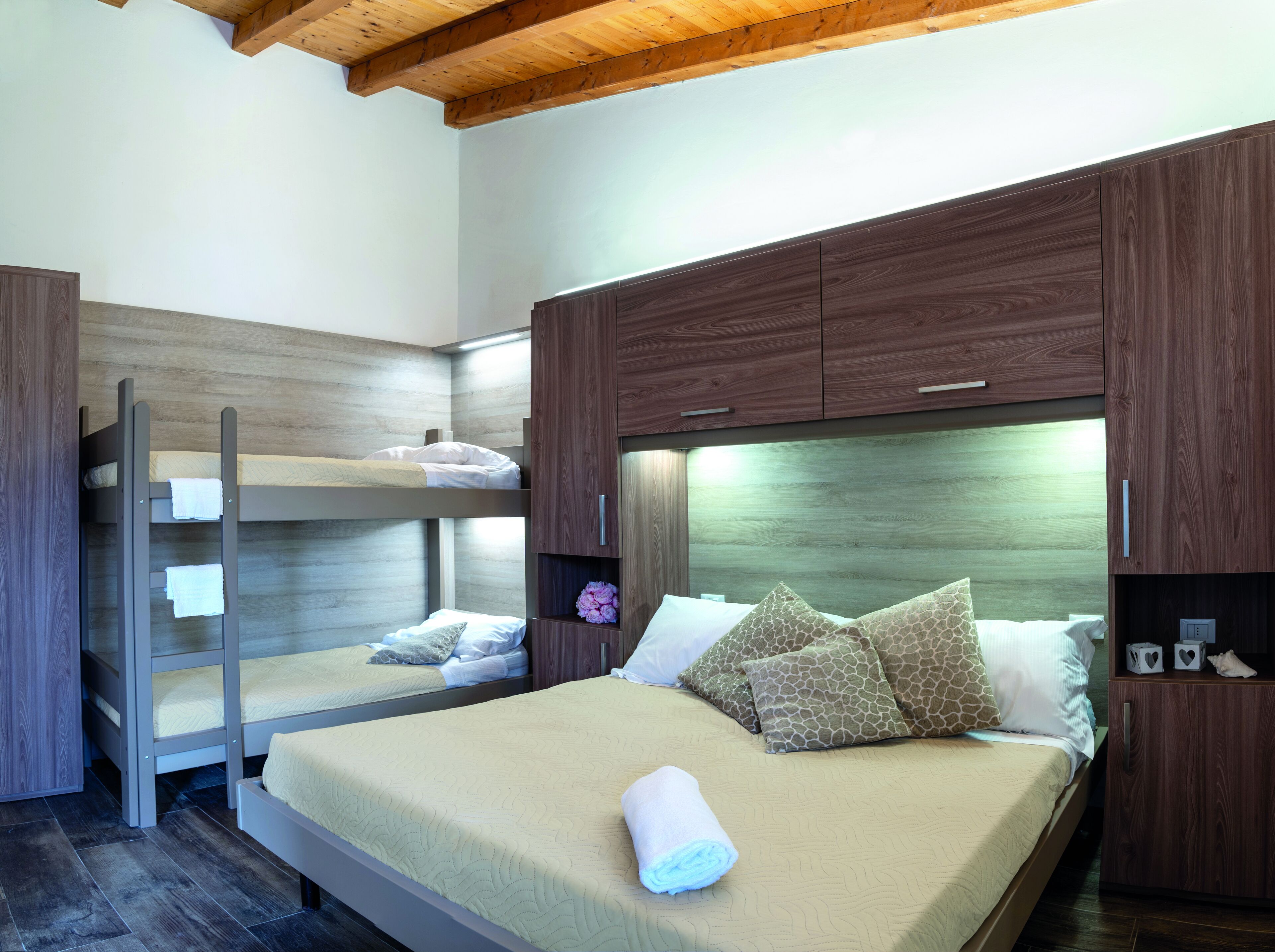 A bunk bed with a wooden headboard, a single bed with a beige bedspread, and a wooden wardrobe.