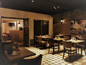 A restaurant with hexagonal patterned flooring, wooden tables and chairs, and a brick wall with a mural. - Hotel Courage Waalkade (Nijmegen)