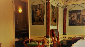 Una habitación de hotel con una cama con dosel, un sillón, una mesita y dos camas.