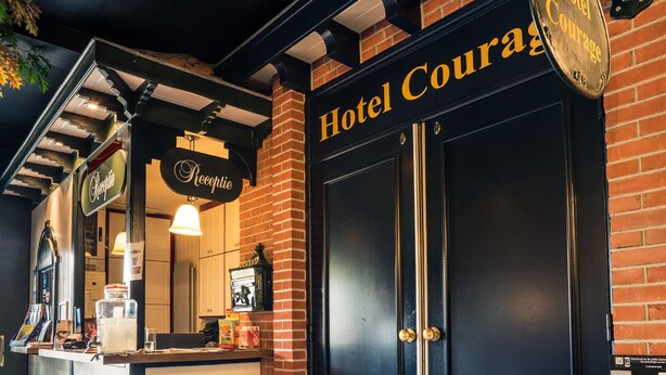 Entrada de hotel con un letrero que dice "Hotel Courage", una recepción y fachada de ladrillo.