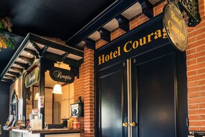 Entrada de hotel con un letrero que dice "Hotel Courage", una recepción y fachada de ladrillo.