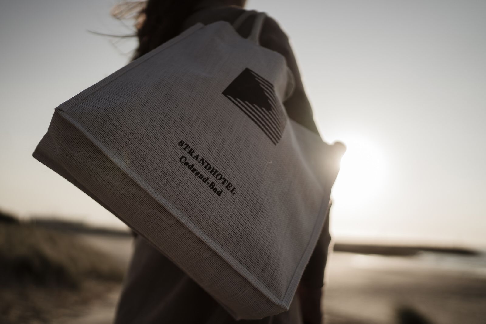 Une personne tenant un sac fourre-tout de marque sur lequel on peut lire l'inscription « STRANDHOTEL Cadzand-Bad ».