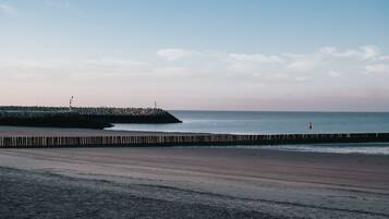 Una playa con un paseo de madera que lleva a un promontorio rocoso.