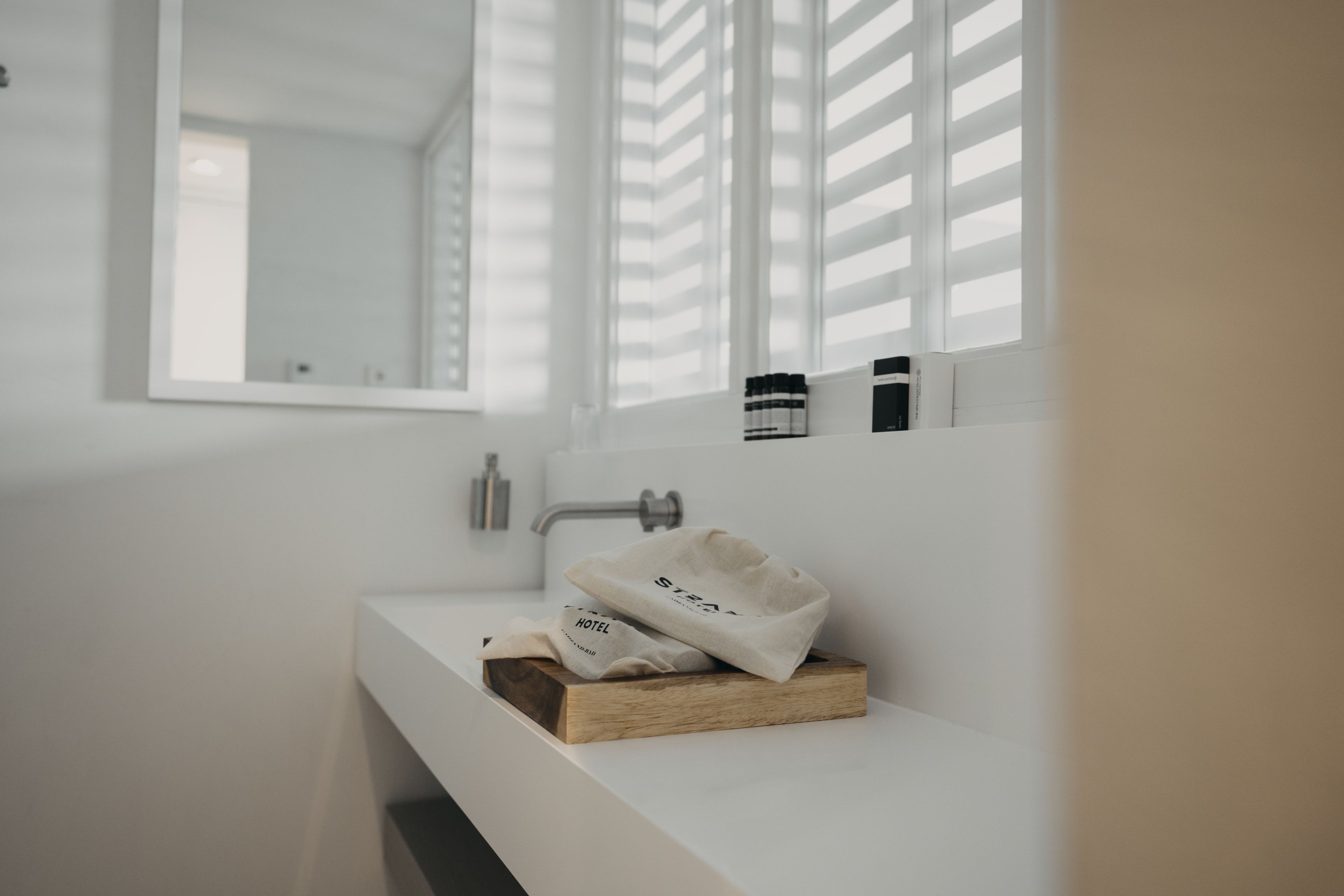 A minimalist bathroom with a white sink, a mirror, and a window with blinds.
