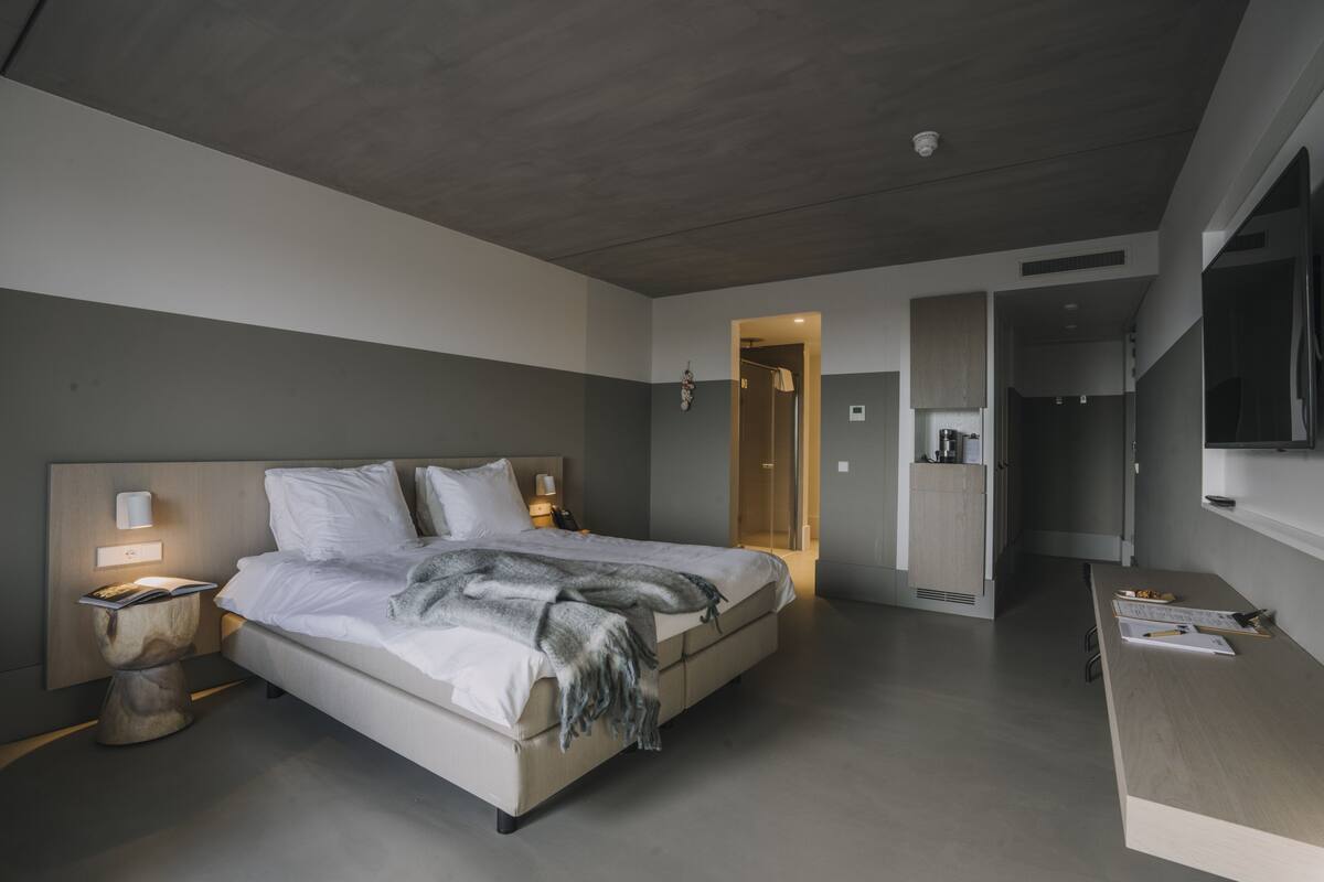 Un dormitorio moderno con una cama grande, lámparas de noche, una mesita de noche de madera y un escritorio con papeles y una computadora portátil.