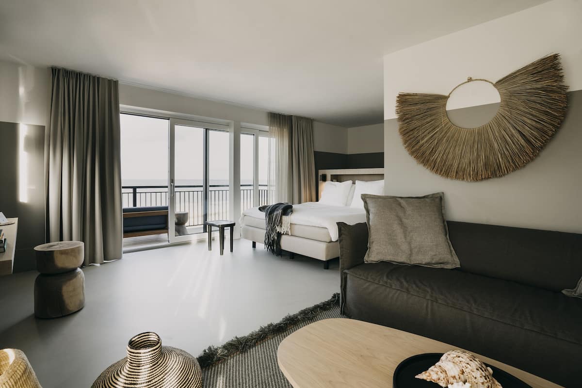 Una habitación de hotel moderna con una cama, un sofá, una mesa de comedor y un balcón con vistas.