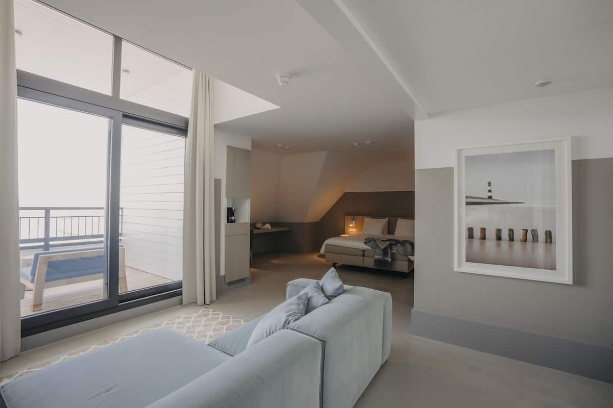 Una habitación de hotel moderna con un balcón grande, un sofá, una cama y un cuadro en la pared.