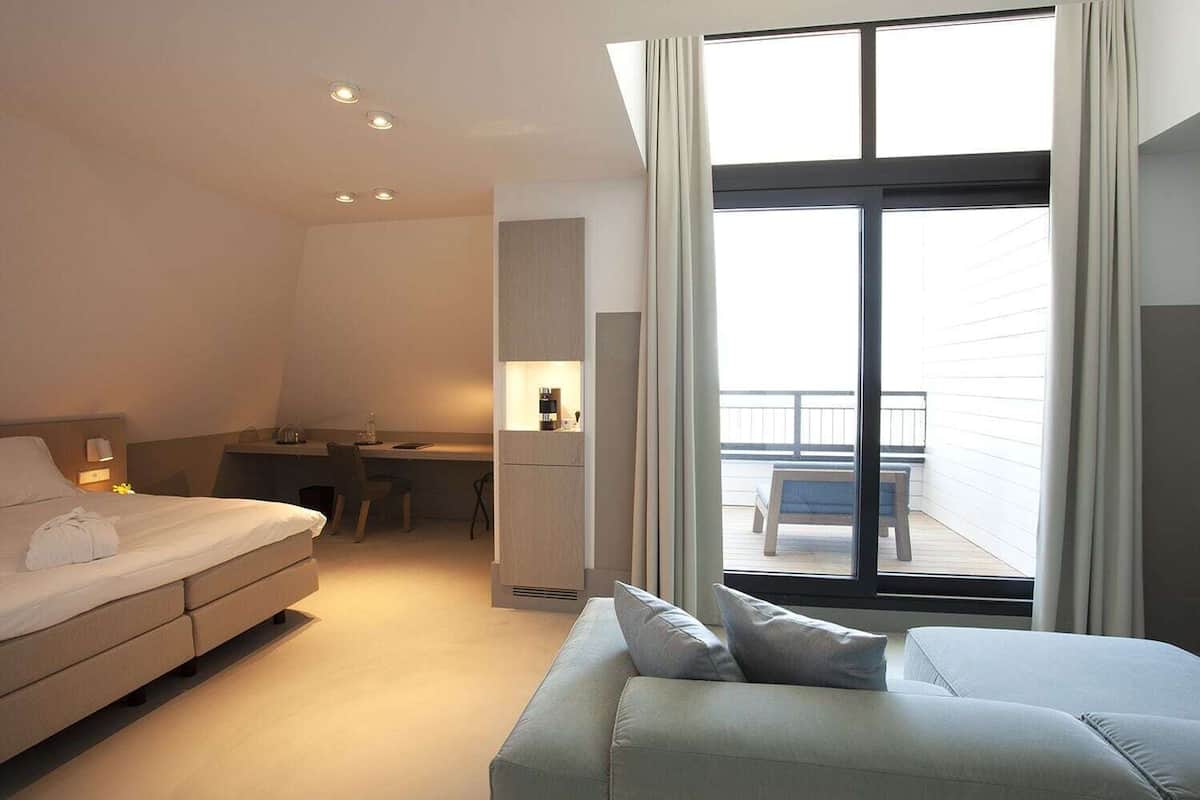 Una habitación de hotel moderna con cama, sofá, escritorio y balcón con vistas.